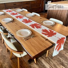 a wooden table with white plates and red maple leaves on the edge, sitting in a kitchen