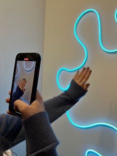 a person holding up a cell phone in front of a neon light sign with their hands