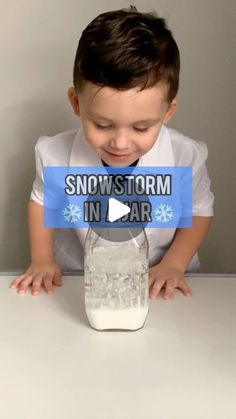 a young boy sitting at a table in front of a jar of snowstorm water