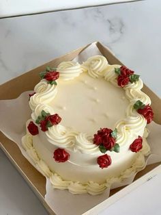 a white frosted cake with red roses on it in a box, ready to be eaten