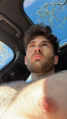 a man with no shirt sitting in the back seat of a car looking up at something