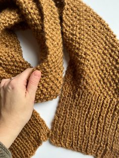 a hand is holding the edge of a knitted scarf