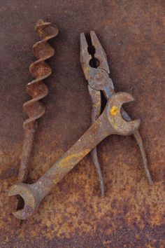 an old rusty wrench sitting on top of a rusted metal table next to a pair of screwdrivers