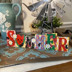 the word summer spelled with colorful letters on a table next to a vase and windmill