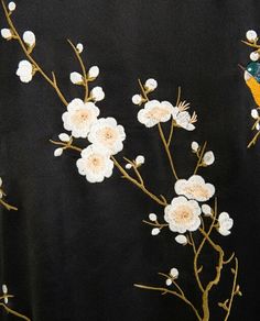 an embroidered black jacket with white flowers and a bird sitting on the branch in front of it