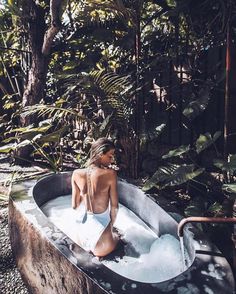 a woman in a white bathing suit sitting in an outdoor hot tub surrounded by trees