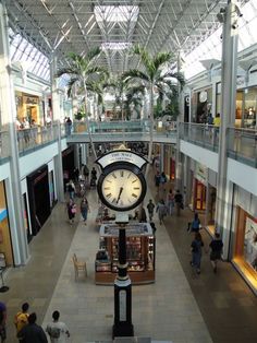 a large clock in the middle of a mall with lots of people walking around it