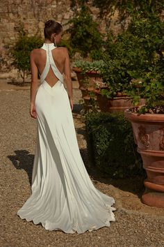 a woman in a white dress standing next to potted plants and looking at the back of her dress