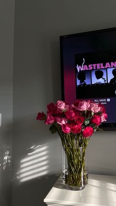 a vase filled with pink roses sitting on top of a white table next to a flat screen tv