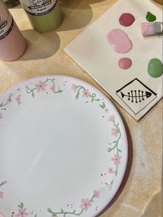 a white plate with pink flowers on it next to some paint and other crafting supplies