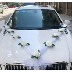 wedding car decorated with white flowers and ribbon on the front hood, along with greenery