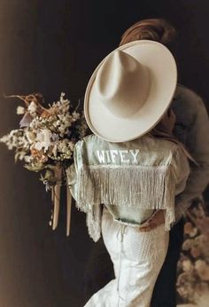 a woman wearing a white cowboy hat and holding a bouquet of flowers in her arms