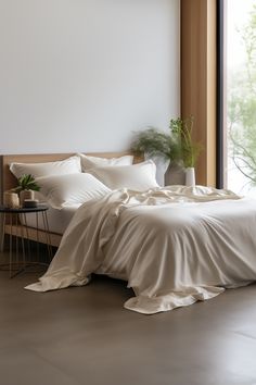 an unmade bed with white sheets and pillows in a room next to a window