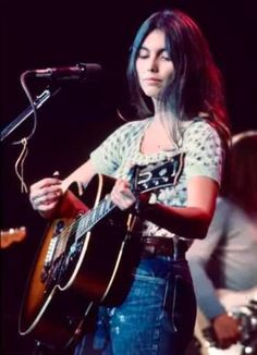 a woman holding a guitar while standing in front of a microphone