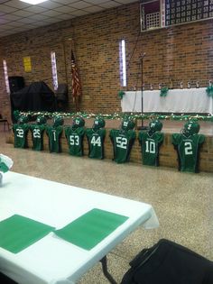 several football jerseys are lined up on the wall in front of a row of tables