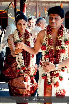 two people dressed in flower leis walking down the street with other people behind them