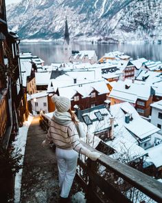 a woman is walking up the stairs in front of snow covered mountains and buildings with a lake below