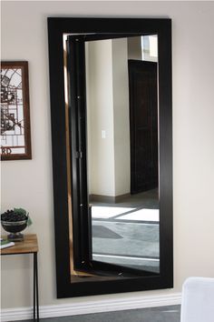 a large black framed mirror sitting on top of a wooden table next to a wall