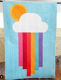 a quilted wall hanging with a rainbow cloud and sun in the sky on it