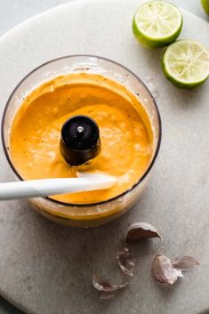 an orange smoothie in a blender with a spoon and limes on the side