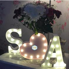 a vase with flowers in it sitting on top of a table next to a light up letter