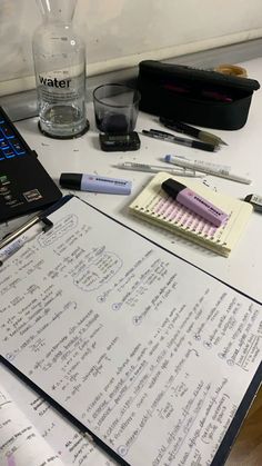 an open notebook sitting on top of a table next to a glass filled with water