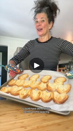 a woman holding a pan full of cookies on top of a wooden table with a video screen