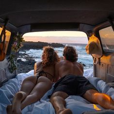 two people laying in the back of a truck looking out at the ocean and rocks