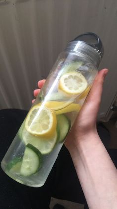 a person holding a water bottle filled with sliced lemons and cucumber slices