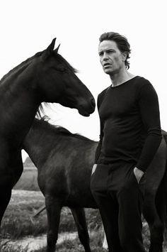 a man standing next to two horses in a field