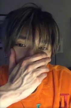 a young man is holding his nose to his mouth and looking at the camera while wearing an orange shirt