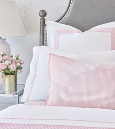 a bed with pink flowers in a vase on the nightstand next to it and a white headboard