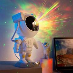 a small toy astronaut is on top of a desk next to a laptop computer and colorful lights