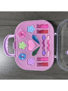 a pink plastic tray filled with lots of different items next to a clear container on top of a wooden table