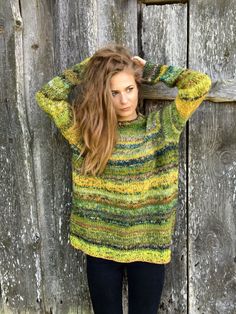 a woman standing in front of a wooden wall wearing a green and yellow striped sweater