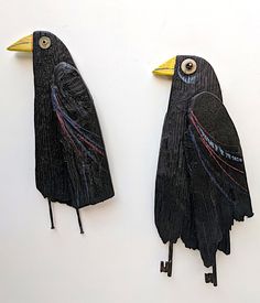 two black birds with yellow beaks are hanging from hooks on a white wall together