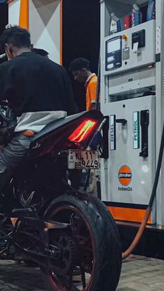 a motorcycle parked in front of a gas station with people filling up the pump area