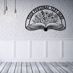 an open book with flowers on it sitting in front of a white brick wall and light bulbs hanging from the ceiling