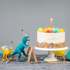 there is a birthday cake with sprinkles on it and two dinosaurs next to it