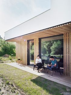 two men sitting in chairs on the side of a building with wood slats covering it