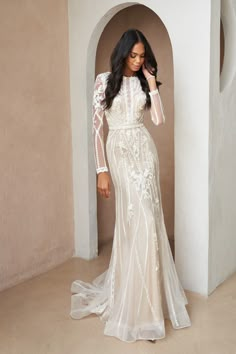 a woman in a white wedding dress standing next to a wall and posing for the camera