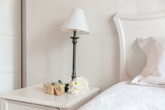 a white nightstand with flowers on it next to a night stand and a small lamp