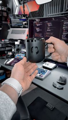 two hands holding a black coffee mug in front of a computer desk