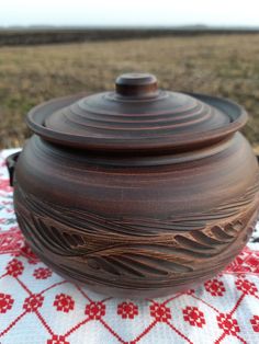 a brown pot sitting on top of a red and white table cloth next to a field