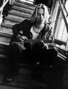 black and white photograph of a woman sitting on stairs playing an acoustic guitar in front of her