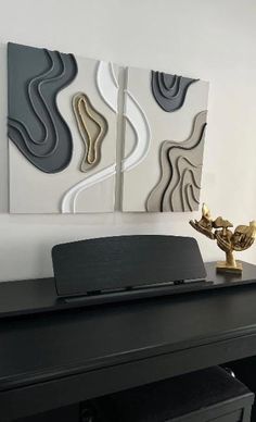 two abstract paintings on the wall behind a black desk with a gold vase in front