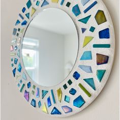 a round mirror with colorful glass pieces on it's side hanging on the wall