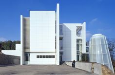 two people are standing in front of a large white building that is on the side of a hill