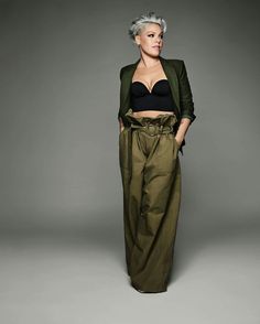 a woman with grey hair wearing green pants and a black bra top is standing in front of a gray background