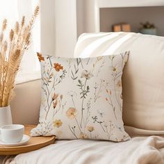 a coffee cup on a tray next to a flowered pillow and some dried grass